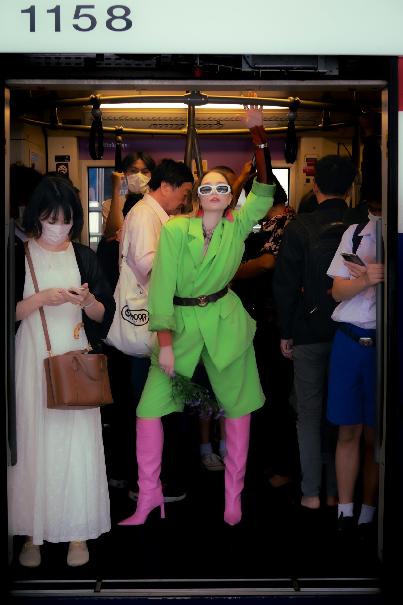 Fashionable woman in a green suit and pink boots on a busy Bangkok metro train.