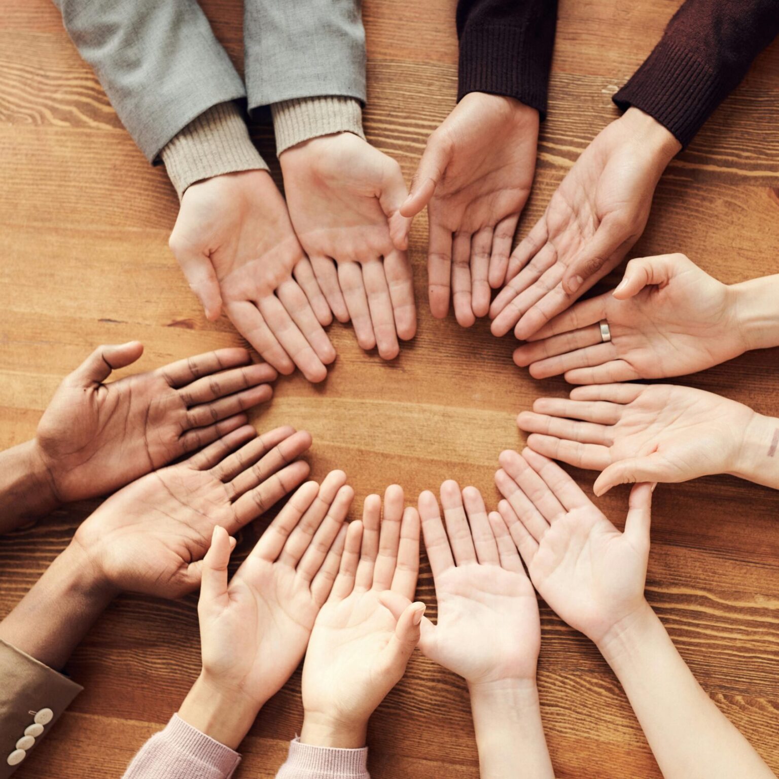 Top view of diverse hands forming a circle on a wooden table, symbolizing unity and diversity.